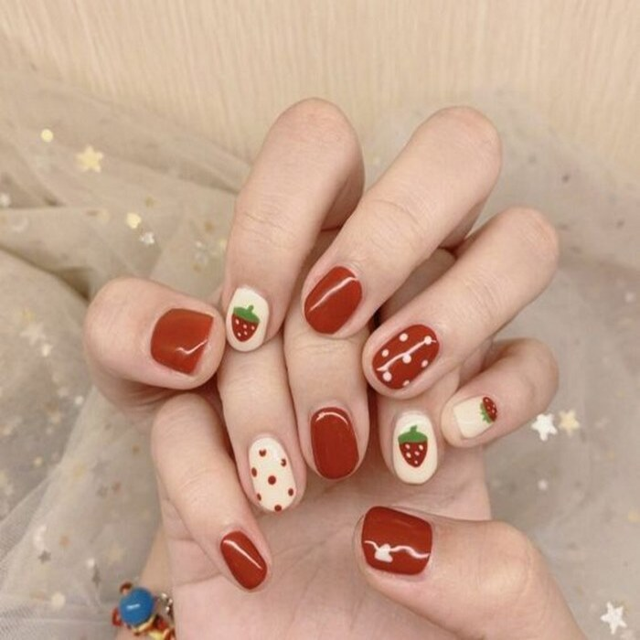 Short red nails painted with strawberries